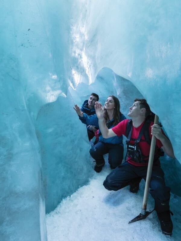 People crouching in ice cave on glacier